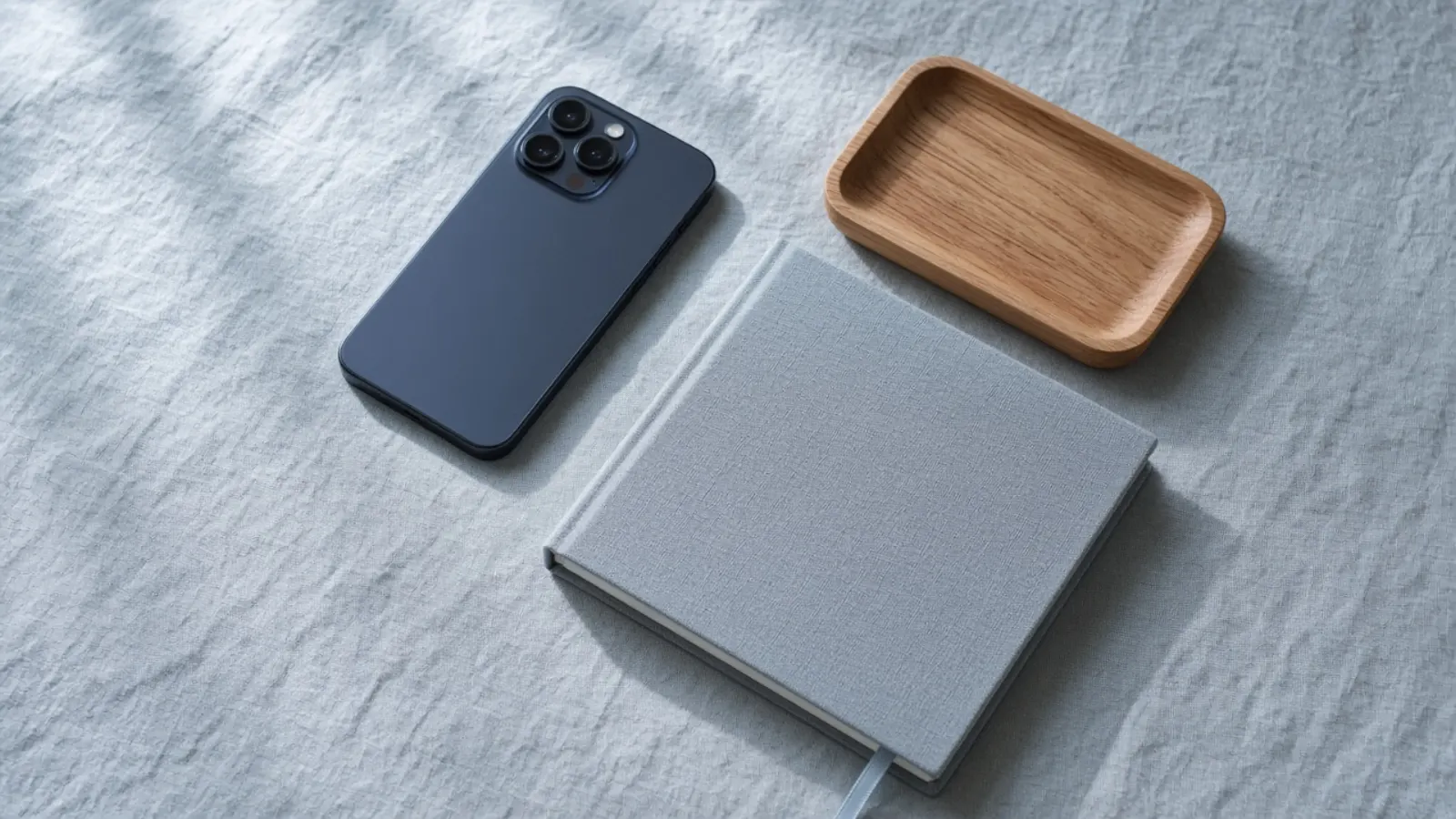 Smartphone face-down with a notebook and wooden tray on a linen table